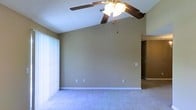 Located at 4401 Beatline Rd. in Long Beach, Mississippi, this single-floor residence offers a welcoming and practical living environment. The main living area is a standout feature of the home, boasting impressively vaulted ceilings that lend a sense of spaciousness and openness to the room. A ceiling fan with an integrated light fixture is centrally mounted, providing both airflow and ambient lighting. The living space is finished with plush wall-to-wall carpeting in a neutral tone, complementing the warm beige walls and crisp white trim throughout. Large vertical blinds on a sliding glass door allow for natural light control while providing access to the outdoors. The open layout flows naturally between areas of the home, with a connecting hallway visible from the main living space, suggesting a thoughtfully designed floor plan. Multiple electrical outlets are positioned conveniently along the walls, adding to the functional design. The textured ceiling adds a classic architectural detail. Overall, this residence presents a clean, neutral palette and airy atmosphere well-suited for comfortable everyday living in the Long Beach community.