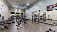 Located at 66 Glenbrook Rd in Stamford, Connecticut, this fitness center is a well-appointed, single-floor facility designed to support a comprehensive workout experience. The main exercise floor is generously sized, featuring durable speckled flooring suited for high-traffic use. A standout design element is the bold, typographic motivational mural that spans an entire accent wall, showcasing fitness-themed phrases in varying fonts against a muted teal-green backdrop, creating an energizing atmosphere throughout the space.

Natural light streams in through multiple windows positioned along the upper walls, complementing the overhead pendant lighting and ceiling fans that ensure the space remains bright and comfortable. The cardio section is well-stocked with a row of treadmills, stationary cycling bikes, and additional cardio machines, all accompanied by wall-mounted flat-screen televisions. A dedicated strength and functional training area features a multi-station cable machine, free weights, medicine balls, and resistance equipment. Glass partitions near the entrance provide visual openness while defining the space, with a staircase visible beyond, adding an architectural dimension. The overall ambiance is clean, modern, and motivating — a fully equipped fitness destination.