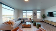 This single-floor residence offers a thoughtfully designed open-concept layout finished with light wood-look flooring throughout. The living area is a standout space, defined by large floor-to-ceiling and oversized windows that frame sweeping views of a waterfront and surrounding cityscape, filling the room with abundant natural light. The living space comfortably accommodates generous seating arrangements and connects seamlessly to the rest of the unit.

The kitchen is well-appointed with warm wood-toned cabinetry extending to the ceiling, stainless steel appliances including a full-size refrigerator, dishwasher, range, and microwave, paired with a textured white tile backsplash and light countertops. An adjacent dining area provides ample space for a full-sized table, making the kitchen zone ideal for both everyday meals and entertaining.

The bedroom is a calm, restful retreat with soft carpet underfoot, a window for natural light, and direct access to a walk-in closet offering practical storage. The bathrooms are clean and functional, featuring light wood-look flooring, warm wood vanity cabinetry, a tub-shower combination, and bright white walls that maintain an airy, modern feel throughout.