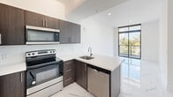This contemporary apartment, located at 1 Curtiss Pkwy in Miami Springs, FL, offers a blend of style and functionality within its 820 square feet. The space is efficiently designed with two bedrooms, including a spacious primary bedroom of 210 square feet, and two bathrooms. The single-story layout encompasses a kitchen, hallway, laundry area, and closet space.

The apartment's most striking feature is its gleaming marble-look tile flooring, which runs throughout the entire space, creating a sense of continuity and luxury. Large windows in the living areas and bedrooms flood the rooms with natural light and provide stunning views of palm trees and water, bringing a touch of tropical paradise indoors.

The kitchen is a highlight, featuring modern dark wood cabinetry contrasted with white quartz countertops. Stainless steel appliances, including a side-by-side refrigerator, built-in microwave, and dishwasher, complete the sleek look. A convenient breakfast bar adds extra prep space and casual dining options.

The bathrooms continue the upscale theme with marble-look tiling, modern vanities, and clean lines. The bedrooms are generously sized, with the primary bedroom offering ample space for a king-sized bed and additional furniture.

Storage is well-considered throughout the apartment, with built-in closets featuring wire shelving systems. The dedicated laundry area adds to the unit's practicality.

Overall, this apartment combines modern aesthetics with practical living, offering a bright, open feel enhanced by its high-end finishes and picturesque Florida views.