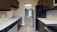 Located at 175 Cousins Dr in Carlisle, Ohio, this two-floor residence offers a practical and comfortable layout with neutral warm-toned walls throughout. The kitchen is a functional galley-style space featuring dark espresso cabinetry, light stone-finish countertops, a stainless steel sink, and black appliances including a refrigerator and dishwasher. Wood-look flooring runs through the kitchen, which opens directly into the main living area. The living and dining spaces are carpeted, with a pendant light fixture overhead and vertical blinds covering a sliding glass door that allows natural light to filter in. Multiple bedrooms are spread across both floors, each finished with plush carpeting, neutral walls, and windows fitted with horizontal blinds. Several bedrooms include sliding or bi-fold closet doors, providing practical storage. A bathroom is also present, featuring a white vanity with cabinetry, a toilet, and wood-look flooring. Textured ceilings are consistent throughout the home. The overall ambiance of the space is clean, understated, and move-in ready, suited for everyday living.