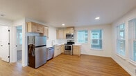 This efficient and thoughtfully designed one-bedroom, one-bathroom unit offers a practical single-floor layout that maximizes every square foot. The open-concept kitchen and living area form the heart of the unit, featuring warm hardwood-style flooring throughout. The kitchen is equipped with light maple cabinetry, white countertops, and a full suite of stainless steel appliances, including a refrigerator, electric range, built-in microwave, and dishwasher. Multiple windows with white blinds flood the space with natural light and provide views of the surrounding neighborhood. The living area opens directly to a private balcony through a glass-paneled door, extending the sense of space outdoors. A stacked washer and dryer unit is conveniently tucked within the living area, adding in-unit laundry functionality. The bedroom offers plush carpeting, two large windows with natural views, and a closet with built-in shelving and a hanging rod. The bathroom is equipped with a single-sink vanity with light wood cabinetry, a tub-shower combination with accessibility grab bars and a fold-down teak bench, and hardwood-style flooring. Clean white walls and recessed lighting throughout lend the unit a bright, modern ambiance.