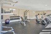 Located at 900 E Saturnino Rd in Palm Springs, California, this fitness center offers a well-appointed exercise space designed to support a comprehensive workout routine. The room features durable speckled rubber flooring throughout, providing a safe and resilient surface suited for a variety of exercises. Recessed lighting illuminates the space evenly, while a wall-mounted mini-split air conditioning unit ensures a comfortable environment year-round — an essential feature in the desert climate of Palm Springs.

The facility is equipped with a thoughtful selection of cardio and strength training equipment. Cardio options include multiple treadmills, an elliptical trainer, and a stationary recumbent bike, offering variety for aerobic workouts. For strength training, the room includes a multi-function cable machine, a power tower for bodyweight exercises, a flat weight bench, and a full dumbbell rack stocked with a range of free weights.

Large glass doors and windows along one wall allow natural light to flood the space and provide views of the surrounding outdoor area, creating an open and energizing atmosphere. The clean white walls and bright, uncluttered layout contribute to a focused and functional workout environment, making this fitness center a practical and well-designed amenity.