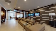 Located at 4190 W 17th Ave in Denver, Colorado, this single-floor amenity space delivers a polished, contemporary environment designed for both relaxation and productivity. The interior showcases a sophisticated design language, blending rich wood paneling, textured tile accent walls, and light hardwood flooring to create a warm yet modern atmosphere throughout.

The centerpiece of the space is a generously sized media lounge, where oversized sectional sofas in neutral tones are arranged facing a striking feature wall clad in dark tile with contrasting light inlays. Three flat-screen televisions are mounted across this wall, making the area ideal for social gatherings or casual entertainment. Sleek metal side tables and a solid wood coffee table add functional elegance to the seating arrangement.

A dedicated conference room provides a professional setting, featuring a substantial live-edge wood table surrounded by high-back upholstered chairs. A dramatic cluster pendant light fixture overhead adds visual interest while providing focused illumination. Wood-paneled walls and patterned wallcovering contribute a refined, executive feel.

Additional areas include a bright entry corridor with floor-to-ceiling glass doors overlooking an outdoor courtyard, a built-in display niche with cabinetry, and a dining area with views to the exterior. Recessed lighting throughout ensures a consistently well-lit and inviting environment.