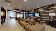 Located at 4190 W 17th Ave in Denver, Colorado, this single-floor amenity space delivers a polished, contemporary environment designed for both relaxation and productivity. The interior showcases a sophisticated design language, blending rich wood paneling, textured tile accent walls, and light hardwood flooring to create a warm yet modern atmosphere throughout.

The centerpiece of the space is a generously sized media lounge, where oversized sectional sofas in neutral tones are arranged facing a striking feature wall clad in dark tile with contrasting light inlays. Three flat-screen televisions are mounted across this wall, making the area ideal for social gatherings or casual entertainment. Sleek metal side tables and a solid wood coffee table add functional elegance to the seating arrangement.

A dedicated conference room provides a professional setting, featuring a substantial live-edge wood table surrounded by high-back upholstered chairs. A dramatic cluster pendant light fixture overhead adds visual interest while providing focused illumination. Wood-paneled walls and patterned wallcovering contribute a refined, executive feel.

Additional areas include a bright entry corridor with floor-to-ceiling glass doors overlooking an outdoor courtyard, a built-in display niche with cabinetry, and a dining area with views to the exterior. Recessed lighting throughout ensures a consistently well-lit and inviting environment.