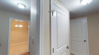This single-floor residence presents a cohesive and functional layout finished in a neutral color palette throughout. The kitchen is equipped with dark-finished cabinetry, dark granite-style countertops, and black appliances including a full-size refrigerator and dishwasher. Wood-look flooring runs through the kitchen, which connects directly to adjacent living areas. The main living space is generously sized, featuring plush carpeting, a sliding glass door with vertical blinds that allows natural light to filter in, and an open flow into a secondary area defined by a partial wall. The bedrooms are carpeted and finished with the same warm neutral tones, each featuring windows with blinds that provide natural light. The bathrooms maintain a consistent design language, featuring dark wood vanities with granite-style countertops, tile flooring, and a tub-shower combination. A mirrored vanity with Hollywood-style lighting is present in one bathroom. Interior doors feature classic raised-panel detailing with brushed nickel hardware. White trim and baseboards provide clean contrast throughout the unit, contributing to a tidy and well-maintained overall presentation.