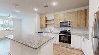This well-designed single-story, 2-bedroom, 3-bathroom home in Atlanta's Moreland Avenue corridor offers a clean, modern aesthetic with consistent light wood flooring and crisp white walls throughout. The open-concept kitchen is a standout feature, showcasing granite countertop surfaces, a central island, white lower cabinetry paired with natural wood-tone upper cabinets, white subway tile backsplash, and a full suite of stainless steel appliances including a range, over-the-range microwave, and dishwasher. The kitchen flows naturally into the main living area, creating a bright, connected living space. The spacious primary bedroom offers a generous footprint and access to its own dedicated bathroom. A secondary bedroom features built-in shelving, adding functional storage and character. Two closets with wire shelving systems provide organized storage solutions. The bathrooms are finished with clean white tile surround tub-shower combinations. A dedicated laundry area houses a full-size top-load washer and dryer. Recessed lighting and ceiling-mounted fixtures illuminate the space throughout. The overall layout, as seen in the 3D model, is efficient and well-proportioned, making excellent use of the available floor area.