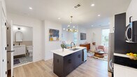 This well-appointed studio offers a smart, open-concept layout that maximizes every square foot across a single floor. The kitchen is a standout feature, anchored by a dark-cabinetry center island topped with a white quartz countertop and an undermount sink. Bar seating along the island makes it ideal for casual dining. Full-height cabinetry — combining dark lower cabinets with crisp white uppers — frames a full suite of stainless steel appliances, including a refrigerator, electric range, and microwave. A brass Sputnik-style chandelier adds a mid-century modern touch overhead, complementing the warm light hardwood flooring that runs throughout the space. Large windows invite abundant natural light into the open living area, which flows seamlessly from the kitchen. The bathroom is elegantly finished with a frameless glass-enclosed walk-in shower featuring vertical subway tile, a mosaic tile floor, matte black fixtures, and a floating vanity with a white countertop. An arched mirror and patterned accent tile floor complete the refined look. Recessed lighting throughout and clean white walls give the entire space a bright, airy ambiance that feels open and inviting.