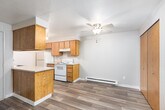 This single-floor residence offers a well-organized layout with a mix of hard-surface and carpeted flooring throughout. The living area serves as the heart of the home, highlighted by a tile-surround fireplace that adds warmth and character to the space. A private entry door opens directly into this area, creating a welcoming transition into the unit. Natural light filters in through windows fitted with vertical blinds, offering views of surrounding greenery.

The galley-style kitchen is efficiently designed, featuring warm wood cabinetry on both upper and lower levels, light countertops, and white appliances including a coil-top range and refrigerator. Wood-look plank flooring runs through the kitchen and adjoining utility areas, providing durability and easy maintenance. A dedicated laundry area with washer and dryer hookups is conveniently tucked nearby.

The bedrooms are carpeted and offer generous wall space, with baseboard heating units ensuring comfort year-round. The bathroom is neatly appointed with a full tub-and-shower combination, a wood-vanity with a speckled countertop, and a mirrored wall. Textured ceilings and neutral warm-toned walls are consistent throughout, giving the space a cohesive and move-in-ready feel.