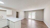 This single-floor, 1-bedroom, 1-bathroom residence offers a thoughtfully organized layout that maximizes its comfortable footprint. The open-concept living area seamlessly connects the kitchen, dining, and living spaces, all finished with durable wood-style flooring and neutral warm-gray walls throughout. The kitchen is well-equipped with stainless steel appliances — including a refrigerator and gas range — white cabinetry, a white quartz peninsula countertop, and recessed lighting overhead, creating a clean and functional cooking space. The living room is bright and airy, highlighted by a set of French doors that invite natural light and provide access to the outdoors. The bedroom features soft carpeting, a ceiling fan with light fixture, and a window that adds additional natural light to the space. The full bathroom includes a tub-shower combination with white surround. A dedicated in-unit laundry room accommodates a full-sized top-loading washer and dryer side by side, complete with overhead wire shelving for added storage. Textured ceilings are present throughout, and the consistent neutral color palette lends a clean, cohesive feel to the entire residence.