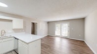 This single-floor, 1-bedroom, 1-bathroom residence offers a thoughtfully organized layout that maximizes its comfortable footprint. The open-concept living area seamlessly connects the kitchen, dining, and living spaces, all finished with durable wood-style flooring and neutral warm-gray walls throughout. The kitchen is well-equipped with stainless steel appliances — including a refrigerator and gas range — white cabinetry, a white quartz peninsula countertop, and recessed lighting overhead, creating a clean and functional cooking space. The living room is bright and airy, highlighted by a set of French doors that invite natural light and provide access to the outdoors. The bedroom features soft carpeting, a ceiling fan with light fixture, and a window that adds additional natural light to the space. The full bathroom includes a tub-shower combination with white surround. A dedicated in-unit laundry room accommodates a full-sized top-loading washer and dryer side by side, complete with overhead wire shelving for added storage. Textured ceilings are present throughout, and the consistent neutral color palette lends a clean, cohesive feel to the entire residence.