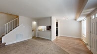 This two-story residence offers a thoughtfully laid-out floor plan across two levels, combining functional design with comfortable living spaces. The main level greets visitors through a paneled front door flanked by transom windows, allowing natural light to fill the entry area, which transitions into a spacious living area with plush wall-to-wall carpeting. Light wood-style flooring extends into the adjacent dining area, creating a natural visual separation between spaces. A pass-through kitchen connects seamlessly to the living area, featuring rich dark cabinetry, granite-style countertops, a stainless steel sink, and black appliances including a refrigerator and electric range. The galley-style kitchen layout maximizes efficiency while maintaining an open feel toward the main living space. A staircase leads to the upper level, where carpeted bedrooms provide a quiet retreat. The primary bedroom is notably spacious, offering dual closets with built-in shelving for ample storage, and is equipped with a ceiling fan. Additional bedrooms also feature ceiling fans and windows with blinds for natural light and privacy. The bathroom presents a clean, neutral aesthetic with large-format tile flooring and classic fixtures. Throughout the home, neutral wall tones and white trim create a cohesive, versatile backdrop.
