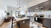 Located at 139 N Dobson Rd in Mesa, AZ, this thoughtfully designed one-bedroom, one-bathroom residence offers a modern aesthetic with high-end finishes across its single floor. Soaring ceilings amplify the sense of space throughout, creating an open and airy atmosphere.

The kitchen is a standout feature, showcasing sleek charcoal-gray cabinetry that extends to ceiling height, a white subway tile backsplash, light quartz countertops, and a full suite of stainless steel appliances including a refrigerator, range, microwave, and dishwasher. A central island with bar seating provides additional prep space and casual dining. Pendant lighting and wood-look flooring complete the contemporary look.

The living area is bright and welcoming, with large sliding glass doors that flood the room with natural light and open to an outdoor space with views of surrounding greenery. The bedroom is a comfortable retreat, featuring tall ceilings and a window that brings in additional natural light. A dedicated closet and in-unit laundry add everyday convenience.

The bathroom is clean and functional, featuring a full tub-shower combination with matte black fixtures and wood-look flooring that ties the space together cohesively.