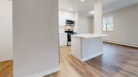 This well-appointed 2-bedroom, 1-bathroom unit at 30 Campbell Crt in Stratford, Ontario offers a thoughtfully designed single-floor layout. Throughout the space, light wood laminate flooring and neutral grey-toned walls create a clean, modern aesthetic that enhances the sense of openness.

The combined kitchen and living area serves as the heart of the unit. The kitchen features crisp white cabinetry with recessed lighting, a white countertop island that provides additional workspace and casual seating, and stainless steel appliances including a refrigerator, range, and microwave. The adjacent living area is bathed in natural light from large windows and a sliding glass door that opens to an outdoor balcony, offering pleasant views of surrounding greenery. Baseboard heating runs along the perimeter of the living space.

Both bedrooms are generously proportioned with large windows that invite natural light. The primary bedroom includes a double-door closet, offering ample storage. The second bedroom features its own window with outdoor views.

The bathroom is finished with large-format beige wall tiles surrounding a full soaker tub and shower, complemented by a white vanity and wood-look flooring. A connecting hallway ties all rooms together efficiently. Textured ceilings are consistent throughout the unit.