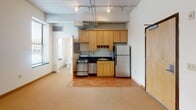 Located at 810 Hennepin Ave in the vibrant heart of Minneapolis, MN, this urban loft-style unit offers a compelling blend of industrial character and functional design. The open-concept layout maximizes the sense of space, with the living and kitchen areas flowing seamlessly together on hardwood flooring that transitions into carpeted zones.

The kitchen is well-appointed with warm maple cabinetry extending to the ceiling for generous storage, dark granite-style countertops, and stainless steel appliances including a gas range and full-size refrigerator. Exposed conduit, ductwork, and a concrete ceiling add an authentic industrial aesthetic throughout, complemented by track lighting that provides practical and stylish illumination.

The sleeping area is carpeted and quietly positioned, benefiting from natural light through a large window with views toward the surrounding urban streetscape. Exposed ceiling infrastructure continues here, reinforcing the loft character of the space.

The bathroom is clean and simply appointed, featuring a full soaking tub and shower combination, pedestal sink, and a round mirror — maintaining a bright, functional aesthetic with white finishes. A wood-paneled entry door adds a warm, modern touch at the entrance. This single-floor unit is ideally situated for those seeking a dynamic urban lifestyle in one of Minneapolis's most walkable corridors.