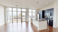 Located in the heart of downtown Green Bay at 115 E Walnut St, this modern one-bedroom, one-bathroom unit offers a well-designed open layout with high-end finishes throughout. The combined kitchen and living area is a standout, featuring rich hardwood flooring, dramatic floor-to-ceiling windows, and direct access to an outdoor balcony that frames sweeping views of the downtown skyline. The kitchen is equipped with dark espresso cabinetry, granite countertops, stainless steel appliances including a refrigerator, range, and microwave, and a large center island with a double undermount sink and stylish pendant lighting overhead. The spacious bedroom continues the floor-to-ceiling window theme, offering abundant natural light and balcony access, and is finished with plush carpeting. A generously sized walk-in closet with built-in shelving and hanging rods provides ample storage. The bathroom is appointed with large-format tile flooring, a full-height tiled walk-in shower with glass doors, a dark-cabinet vanity, and a wide mirror with overhead lighting. The unit's modern aesthetic, abundant natural light, and elevated city views make it a compelling urban living space in downtown Green Bay.