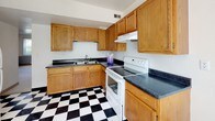 Located at 1201 E San Miguel St in Colorado Springs, Colorado, this single-floor unit offers a straightforward and functional layout designed for comfortable everyday living. The kitchen is a standout area, featuring warm oak cabinetry that extends from floor to ceiling, dark speckled countertops, and a bold black-and-white checkered tile floor that adds a classic, timeless character to the space. A white electric range with a ventilation hood, a double-basin sink, and generous upper and lower cabinet storage round out the kitchen's practical design. The bedrooms are finished with neutral wall-to-wall carpeting and feature a two-tone paint scheme — white above and soft blue-gray below — creating a calm, understated atmosphere. One bedroom includes a built-in closet with bi-fold doors and overhead lighting, while large windows with vertical blinds allow natural light to fill the rooms. The bathroom continues the black-and-white tile theme and is outfitted with a full soaking tub and shower combination with white subway tile surround and chrome fixtures. The overall aesthetic of the unit is clean and practical, making it a solid, move-in-ready space in a residential Colorado Springs neighborhood.