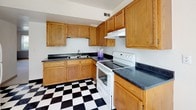 Located at 1201 E San Miguel St in Colorado Springs, Colorado, this single-floor unit offers a straightforward and functional layout designed for comfortable everyday living. The kitchen is a standout area, featuring warm oak cabinetry that extends from floor to ceiling, dark speckled countertops, and a bold black-and-white checkered tile floor that adds a classic, timeless character to the space. A white electric range with a ventilation hood, a double-basin sink, and generous upper and lower cabinet storage round out the kitchen's practical design. The bedrooms are finished with neutral wall-to-wall carpeting and feature a two-tone paint scheme — white above and soft blue-gray below — creating a calm, understated atmosphere. One bedroom includes a built-in closet with bi-fold doors and overhead lighting, while large windows with vertical blinds allow natural light to fill the rooms. The bathroom continues the black-and-white tile theme and is outfitted with a full soaking tub and shower combination with white subway tile surround and chrome fixtures. The overall aesthetic of the unit is clean and practical, making it a solid, move-in-ready space in a residential Colorado Springs neighborhood.