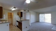 This single-floor residence features an open and functional layout that connects the kitchen and living area seamlessly. The kitchen is equipped with warm wood-toned cabinetry, a built-in dishwasher, a refrigerator, and a peninsula with a sink that overlooks the main living space — ideal for both cooking and casual interaction. Tile flooring in the kitchen transitions into plush carpeting throughout the living area, adding a comfortable and inviting feel underfoot.

Vaulted ceilings lend a sense of openness and height to the space, while a ceiling fan with a light fixture helps maintain airflow and comfort. Recessed HVAC vents are integrated into the ceiling, ensuring efficient climate control throughout. The textured ceiling adds a classic residential character to the interior.

The living area is bright and airy, benefiting from natural light that streams in through a large sliding glass door fitted with vertical blinds, which leads to an outdoor area. A passthrough hallway connects to additional areas of the unit, providing a practical flow between spaces. Overall, the layout is straightforward and well-organized, making efficient use of the available space while maintaining a welcoming atmosphere.