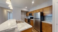 Located at 941 Taylor Station Rd in Gahanna, Ohio, this single-floor residence offers a thoughtfully designed layout with modern finishes throughout. The kitchen serves as a functional centerpiece, showcasing warm honey-toned cabinetry, marble-look countertops, and a full suite of stainless steel appliances including a refrigerator, range, and built-in microwave. A peninsula with pendant lighting overhead provides additional prep space and casual seating, while hardwood-style flooring ties the kitchen and adjacent areas together seamlessly. A double-basin sink and dishwasher add to the kitchen's practicality. The bedrooms feature neutral-toned carpet and windows fitted with blinds that allow natural light to filter in, creating a calm and comfortable atmosphere. Two bathrooms serve the residence, each outfitted with warm wood vanities, marble-look countertops, and hardwood-style flooring. One bathroom includes a walk-in shower with a glass enclosure, while the other features a tub-shower combination. The overall color palette of soft grays and warm wood tones lends the space a clean, cohesive aesthetic. Recessed lighting throughout maintains a bright and welcoming ambiance across the single-level floor plan.