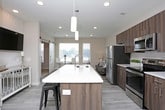 This thoughtfully designed single-floor residence offers a seamless blend of modern aesthetics and everyday functionality. The open-concept kitchen and living area serves as the heart of the home, featuring light wood-look flooring, recessed lighting, and a smooth flow between spaces. The kitchen is outfitted with stainless steel appliances, including a refrigerator, range, and over-the-range microwave, complemented by rich walnut-toned cabinetry and crisp white countertops. A central island with bar seating provides additional prep space and a casual dining option, while pendant lighting adds a stylish finishing touch. The living area benefits from natural light streaming through multiple windows, creating a bright and welcoming atmosphere. The bedroom is a calm retreat, finished with plush carpeting, soft neutral walls, and a window that brings in natural light. The bathroom is clean and well-proportioned, featuring wood-look tile flooring, a vanity with walnut cabinetry, and a full tub-shower combination. A dedicated in-unit laundry area with a stacked washer and dryer is conveniently located adjacent to the bathroom, along with built-in shelving for extra storage. Neutral tones and cohesive finishes throughout give the space a polished, move-in-ready feel.