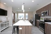 This thoughtfully designed single-floor residence offers a seamless blend of modern aesthetics and everyday functionality. The open-concept kitchen and living area serves as the heart of the home, featuring light wood-look flooring, recessed lighting, and a smooth flow between spaces. The kitchen is outfitted with stainless steel appliances, including a refrigerator, range, and over-the-range microwave, complemented by rich walnut-toned cabinetry and crisp white countertops. A central island with bar seating provides additional prep space and a casual dining option, while pendant lighting adds a stylish finishing touch. The living area benefits from natural light streaming through multiple windows, creating a bright and welcoming atmosphere. The bedroom is a calm retreat, finished with plush carpeting, soft neutral walls, and a window that brings in natural light. The bathroom is clean and well-proportioned, featuring wood-look tile flooring, a vanity with walnut cabinetry, and a full tub-shower combination. A dedicated in-unit laundry area with a stacked washer and dryer is conveniently located adjacent to the bathroom, along with built-in shelving for extra storage. Neutral tones and cohesive finishes throughout give the space a polished, move-in-ready feel.