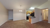 This single-floor unit at Austin Park Apartments offers a well-designed open-concept layout that maximizes the sense of space throughout. The living and dining area is a standout, boasting soaring vaulted ceilings fitted with a ceiling fan and a decorative chandelier, creating an airy and open ambiance. Plush wall-to-wall carpeting runs throughout the living spaces, adding warmth and comfort underfoot. A sliding glass door floods the living room with natural light and provides outdoor access.

The kitchen is thoughtfully arranged with light wood cabinetry, dark granite-style countertops, and black appliances including a refrigerator, electric range, and sink. A peninsula breakfast bar connects the kitchen to the living and dining area, offering a practical space for casual dining or food preparation. The kitchen features tile flooring, providing easy maintenance in this high-traffic area.

The bedroom is a generously sized, carpeted retreat featuring a tray ceiling detail, a ceiling fan, and a window fitted with blinds for natural light and privacy. An expansive walk-in closet off the bedroom provides abundant storage with wire shelving along multiple walls. The bathroom is clean and functional, complete with tile flooring, a full soaking tub with shower, and ample space for everyday needs.