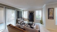 Located on Cassanna Way in Oceanside, California, this single-story residence offers a comfortable and well-organized floor plan with multiple living spaces designed for everyday functionality. The living room is bright and welcoming, featuring large windows with vertical blinds that invite natural light, soft carpet underfoot, crown molding details, and a built-in shelving niche — creating a versatile space for relaxing or entertaining. The kitchen is efficiently laid out with white cabinetry, a double-basin sink set into a smooth countertop with a pass-through bar, a full suite of appliances, and a skylight-style ceiling fixture that keeps the space well-lit. Multiple bedrooms are carpeted and share a consistent, neutral aesthetic, each equipped with ceiling fans with light fixtures and windows that bring in natural light. The primary bedroom includes a large window with an outdoor view and ample dresser space. The bathrooms feature wide vanity countertops with generous cabinet storage below, large mirrors, and bright overhead lighting. One bathroom offers a dual-sink vanity and a separate bathing area. Throughout the home, a consistent warm, neutral color palette and textured ceilings contribute to a calm and cohesive ambiance.