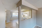 This three-bedroom, one-bathroom home in Edmonton's north side spans three floors, offering a well-distributed and functional layout. Light-toned hardwood flooring runs throughout the main and upper levels, complementing the neutral warm-grey walls and textured ceilings that give the space a clean, understated character. The main floor features an open-concept living and dining area with natural light from street-facing windows, flowing into a compact kitchen. The kitchen is equipped with white cabinetry, a tile backsplash, electric range, refrigerator, and track lighting overhead, with a pass-through opening that connects it visually to the living area. A balcony extends the living space outdoors. The upper floor houses the bedrooms, each with sliding-door closets providing ample storage. The primary bedroom offers a comfortable footprint with a dedicated closet. The full bathroom is a standout feature, finished with large marble-patterned wall tiles surrounding a soaker tub-shower combination, giving it a refined, spa-like appearance. The unfinished basement level presents an open canvas with built-in wood shelving units and a separate closet space, ideal for storage or future development. Multiple hallways and four closets throughout the home add further practicality to this well-structured multi-floor property.