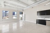 Located in the heart of Downtown Los Angeles on South Spring Street, this urban loft delivers a compelling blend of industrial character and modern finishes. The open-concept main living area is defined by soaring exposed concrete ceilings with visible structural beams and bold silver ductwork, lending an authentic loft aesthetic. Polished light-toned tile floors run throughout, reflecting natural light and enhancing the sense of openness. Large windows frame dynamic city skyline views, and a glass-panel door opens to a private balcony, seamlessly connecting the interior to the vibrant urban landscape outside.

The kitchen is thoughtfully designed with dark espresso cabinetry reaching to the ceiling, white countertops, a clean tile backsplash, and a full suite of stainless steel appliances including a refrigerator, range, microwave, and dishwasher — offering both style and practicality.

The bathroom features a full soaking tub and shower adorned with striking blue and gray mosaic glass tile, complemented by a vessel sink set on a dark vanity with a marble-toned countertop, chrome fixtures, and a large mirror — creating a spa-like retreat. The overall ambiance of the space is bright, airy, and distinctly metropolitan, ideal for those seeking an elevated Downtown Los Angeles lifestyle.