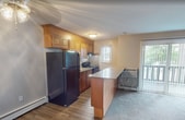 Located on Fairfax Drive in Warwick, Rhode Island, this 570-square-foot, single-floor apartment offers a practical and comfortable layout across one bedroom and one bathroom. The open-concept kitchen and living area serves as the heart of the unit, featuring wood-toned cabinetry, a granite-topped kitchen island, black appliances including a refrigerator and gas range, and durable hardwood-style flooring that transitions into plush carpeting in the living space. A sliding glass door provides direct access to a private outdoor balcony and allows natural light to fill the room. Baseboard heating runs throughout the unit, ensuring consistent warmth. The 170-square-foot bedroom is finished with neutral-toned walls, wall-to-wall carpeting, and baseboard heating, offering a quiet and restful retreat. The bathroom features a full tub and shower combination with white tile surround, chrome fixtures, a wood-framed vanity with a granite countertop, an undermount sink, and a well-lit mirror. Clean, neutral paint tones are carried throughout the apartment, creating a cohesive and move-in-ready atmosphere suited for individuals or couples seeking a functional home in Warwick, RI.
