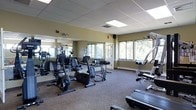 This single-floor amenity space offers a thoughtfully arranged layout encompassing several distinct functional areas. The fitness center is a standout feature, generously sized and equipped with a variety of cardio and strength training machines, including stationary bikes, ellipticals, and weight equipment. Large windows along multiple walls flood the room with natural light and provide views of surrounding greenery, while floor-to-ceiling mirrors enhance the sense of openness. A drop ceiling with recessed lighting completes the professional feel of the space.

Adjacent to the fitness center is a billiards room, centered around a full-size pool table that serves as an inviting focal point for recreation and socializing. The lounge area provides a comfortable gathering space furnished with seating arrangements that encourage relaxation and conversation. Warm, neutral tones and carpeted flooring carry throughout much of the space, contributing to a welcoming ambiance.

A dedicated laundry facility rounds out the amenities, featuring a long row of side-by-side machines that offer residents convenient on-site laundering. The overall layout is practical and well-organized, with clearly defined zones that cater to fitness, leisure, and everyday living needs within a single, cohesive level.