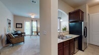 This single-floor residence offers a thoughtfully designed layout that balances comfort and functionality. The open-concept living area is bright and welcoming, featuring plush carpeted flooring, a ceiling fan, and a glass-paneled door that fills the space with natural light and provides access to an outdoor area. The room offers ample space for seating and is finished with warm neutral tones that carry throughout the home.

The galley-style kitchen is a standout feature, equipped with rich dark-wood cabinetry, granite countertops, a dual-basin stainless steel sink, and stainless steel appliances including a refrigerator, electric range, and built-in microwave. A decorative arched pass-through connects the kitchen to the living area, enhancing the open feel of the floor plan. Tile flooring in the kitchen provides both durability and easy maintenance.

The residence includes two carpeted bedrooms, each offering a calm, restful atmosphere. Both rooms feature soft neutral walls, and one benefits from a large window that invites natural light. Closet access is conveniently located in each room.

The bathroom is finished with tile flooring and tile-surround tub and shower combination, complemented by dark-wood vanity cabinetry and a clean, understated countertop. Every detail of this home reflects a cohesive and practical design aesthetic.