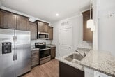 This 680-square-foot, one-bedroom, one-bathroom apartment at 2015 Wave Crest Drive in Brentwood, NC offers a well-designed single-floor layout with modern finishes throughout. The open-concept kitchen and living area serves as the heart of the unit, featuring dark espresso cabinetry with brushed nickel hardware, granite countertops, stainless steel appliances including a French door refrigerator, microwave, and range, pendant lighting, and a breakfast bar peninsula ideal for casual dining. Wood-look luxury vinyl plank flooring runs throughout the entire unit, complemented by crisp white baseboards and crown molding in the main living areas. The living room is bright and spacious, with ceiling fan, natural light from multiple windows, and direct access to a private balcony. The 150-square-foot bedroom features a ceiling fan, generous natural light, and connects to a walk-in closet outfitted with wire shelving systems. The bathroom includes a full tub/shower combo, dark wood vanity with granite countertop, and matching LVP flooring. A dedicated laundry area houses a full-size washer and dryer with overhead cabinetry for additional storage. The unit's neutral gray palette and clean architectural details create a cohesive, modern aesthetic.