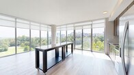 Located at 8231 Crestwood Heights Drive in McLean, VA, this modern 2-bedroom, 2-bathroom residence offers a thoughtfully designed single-floor layout that maximizes natural light and outdoor views. The open-concept living and kitchen area is anchored by dramatic floor-to-ceiling glass windows that frame sweeping panoramas of manicured green spaces and the surrounding cityscape. Light hardwood flooring runs throughout, complementing the clean, neutral palette of the interiors. The kitchen is outfitted with rich warm-toned cabinetry, granite countertops, and stainless steel appliances, including a range, microwave, and dishwasher. Both bedrooms are generously sized, each featuring large windows that flood the rooms with natural light and offer picturesque outdoor views. The spacious primary bedroom provides ample room for comfortable furnishings. Two hallways connect the living spaces to the bedrooms and closets, ensuring a practical and efficient flow. Each bathroom is well-appointed with granite-topped dark wood vanities and tile flooring; one bathroom features a walk-in shower, while the other includes a full soaking tub. Two dedicated closets provide substantial storage. Recessed lighting throughout adds a polished finishing touch to this bright, contemporary residence.