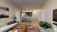 Located at 4111 E Ninth Ave in Denver's vibrant East Colfax neighborhood, this contemporary single-floor residence offers a thoughtfully designed open-concept layout finished with light wood-tone flooring throughout the main living areas. The spacious living room is anchored by large windows and a sliding glass door that open to a private balcony with urban views, filling the space with natural light. Pendant lighting and a built-in shelving nook add character to the living and dining area.

The kitchen is a standout feature, showcasing dark cabinetry with a contrasting white quartz countertop, stainless steel appliances including a refrigerator, microwave, and range, and a generous island with bar seating for four — ideal for casual dining and entertaining. A dedicated workspace or utility corridor runs alongside the kitchen, providing additional storage and prep space.

The bedrooms are well-appointed retreats, each with plush carpeting, large windows, and ample room for full furniture arrangements. The bathrooms are finished with large-format gray tile, including a soaking tub with tiled surround, and dark-toned vanity cabinetry with framed mirrors. A separate water closet adds convenience. The overall design palette is neutral and modern, creating a clean, cohesive aesthetic throughout.