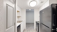 This well-maintained single-floor unit offers a thoughtfully laid-out interior finished with a clean, neutral palette throughout. The galley-style kitchen is efficiently designed, featuring white cabinetry, marble-look countertops, a stainless steel sink, a dishwasher, an electric range with overhead ventilation, and a stainless steel refrigerator. Light wood-look vinyl plank flooring runs through the kitchen and connects seamlessly to the adjacent living area, creating a cohesive flow between spaces. The living area is bright and open, with crisp white walls and ample room for a variety of furniture arrangements. The bedroom is carpeted for added comfort and warmth, and includes a ceiling fan with a light fixture and a window fitted with blinds that allows natural light to filter in. The bathroom is neatly appointed with a marble-look vanity countertop, a full tub-shower combo with a curved curtain rod, wood-look tile flooring, and brushed nickel hardware and fixtures throughout. Textured ceilings are present in the kitchen area, while smooth finishes carry through the rest of the unit. The overall ambiance is clean, functional, and move-in ready.