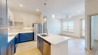 This single-floor residence offers 2 bedrooms and 3 bathrooms within a thoughtfully designed, open-concept layout. Light wood-tone flooring runs throughout, creating a cohesive and airy feel across every room.

The kitchen is a standout feature, showcasing a two-tone design with navy blue lower cabinetry paired with white upper cabinets, complemented by a marble-style tile backsplash. A large center island with a white quartz countertop and integrated sink serves as a functional focal point, while pendant lighting and stainless steel appliances—including a refrigerator, range, and microwave—complete the space. The kitchen flows seamlessly into the living area, which benefits from natural light through windows overlooking an exterior balcony railing, and is equipped with a ceiling fan.

The bedrooms feature light wood flooring, neutral white walls, and window blinds that allow adjustable natural light. The primary bedroom includes a walk-in closet with built-in hanging rods and shelving. The bathrooms are finished with marble-style tile surrounds, soaking tub-shower combinations, and open shelving. A dedicated laundry area houses a full-size side-by-side washer and dryer, adding everyday convenience.