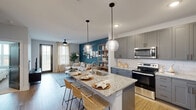 Located at 401 Lime Quarry Rd in Madison, Alabama, this single-floor residence offers a well-appointed open-concept layout that seamlessly connects the kitchen, dining, and living areas. The kitchen is a standout feature, equipped with grey shaker-style cabinetry, a white subway tile backsplash, stainless steel appliances, and a granite-topped island with an undermount sink and bar seating, illuminated by striking globe pendant lights. Wood-look flooring flows throughout the main living areas, adding warmth and continuity to the design. The living room is anchored by a bold teal accent wall adorned with a curated gallery arrangement, complemented by a ceiling fan and a glass door that invites natural light and outdoor views. The bedroom features decorative wallpaper, a ceiling fan, and a window with outdoor views, creating a bright and serene retreat. Two bathrooms echo the home's design language with granite countertops and grey cabinetry; one offers a walk-in shower with tile surround, while the other includes a tub-shower combo and direct access to a spacious walk-in closet with ample rod and shelf storage. Throughout, the cohesive palette of grey, white, and teal tones creates a modern yet inviting atmosphere.