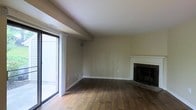 This two-floor space features a well-appointed main living area that showcases warm hardwood flooring throughout, creating a cohesive and inviting atmosphere. A standout feature of the living room is the classic fireplace framed by a clean white mantel with a dark stone hearth, serving as a natural focal point for the room. The neutral-toned walls provide a versatile backdrop, complementing the warm wood floors and offering flexibility for various interior styles. A large sliding glass door on one side of the living area floods the space with natural light while providing direct access to an exterior area, enhancing the connection between indoor and outdoor spaces. The sliding door also offers views of the adjacent exterior, adding depth to the room. Vented HVAC registers are visible in the ceiling and walls, indicating a centralized climate control system throughout. The overall ambiance of the main level is open and functional, with clean lines and practical finishes. The property extends to a second floor, providing additional living space beyond the main level. The combination of the fireplace, natural light, and hardwood flooring gives the space a comfortable and classic character.
