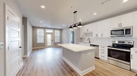 Located in Charlotte's vibrant Dilworth neighborhood, this well-appointed 2-bedroom, 3-bathroom residence offers a clean, contemporary aesthetic with consistent finishes throughout. The open-concept kitchen and living area serves as the heart of the home, anchored by a central island with white quartz countertops, crisp white cabinetry with matte black hardware, a subway tile backsplash, and stainless steel appliances. Industrial-style pendant lighting adds a stylish focal point overhead, while recessed lighting and light-toned hardwood flooring extend throughout the space. The living area benefits from natural light through large windows and a glass-paned door. Both bedrooms are bright and well-proportioned, each featuring large windows with blinds, ceiling fans, and the same warm hardwood flooring. The primary bedroom connects to an en-suite bath offering a white vanity with quartz countertop, a framed mirror, and a glass-enclosed tiled walk-in shower, plus access to a spacious walk-in closet with wire shelving. Two additional bathrooms and a second closet provide ample storage and convenience. Neutral gray walls, clean white trim, and modern fixtures create a cohesive, move-in-ready atmosphere throughout.
