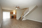This two-story home offers a well-organized layout designed for comfortable everyday living. The main level features an open living area with rich, dark hardwood-style flooring and a ceiling fan overhead, creating a bright and airy atmosphere. A staircase with a classic white baluster railing connects seamlessly to the upper level. The kitchen is well-appointed with warm honey-toned wood cabinetry, light countertops, a double sink, and black and stainless steel appliances including a range, microwave, and refrigerator. Track lighting overhead enhances the functional workspace, and vertical blinds offer adjustable natural light.

The upper level hosts multiple carpeted bedrooms, each featuring ceiling fans and window blinds that allow for natural light. One bedroom includes mirrored sliding closet doors, while the primary bedroom features a dedicated closet and direct access to a private bathroom. A staircase landing provides convenient access between rooms. The bathrooms throughout the home are consistent in finish, each featuring warm wood vanity cabinetry, white countertops with an integrated sink, chrome fixtures, and a lighted mirror above. The textured walls add subtle depth to each bathroom's design. Overall, the home presents a clean, neutral palette throughout its two floors.