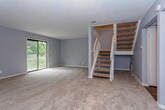This two-story home offers a thoughtfully arranged layout spread across two levels, connected by a classic staircase with white wood railings and natural wood treads. The main level features a generously sized living room finished with plush carpet, neutral gray walls, and a fireplace set against a bold accent wall — a natural focal point for the space. A sliding glass door bathes the room in natural light and provides access to an outdoor area. Adjacent to the living room, the galley-style kitchen is well-equipped with rich, dark wood cabinetry, dark granite-style countertops, wood-look vinyl flooring, and black appliances including a refrigerator, electric range, and dishwasher. The main level also includes a bathroom with wood-look flooring and built-in storage. Upstairs, the bedrooms are carpeted and finished with the same soft gray tones, each featuring ceiling fans with light fixtures and windows fitted with horizontal blinds that allow natural light to filter in. The upper-level bathroom offers a tiled shower-tub combination, wood-look flooring, and a vanity with a light countertop. Textured walls and ceilings throughout add a layer of classic character to the overall design of this comfortable, move-in-ready home.