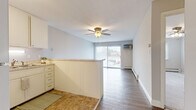 Located at 212 Thompson Ave W in West St. Paul, MN, this one-bedroom, one-bathroom unit offers a practical and well-organized single-floor layout. The kitchen is designed in a U-shape configuration, featuring white cabinetry extending to the ceiling, light stone-toned countertops, white appliances including a refrigerator and range, and tile flooring. A half-wall peninsula connects the kitchen to the adjoining living area, creating an open sightline throughout the space. The living area features durable wood-style flooring, a ceiling fan with light fixture, a wall-mounted air conditioning unit, and a sliding glass door that allows natural light to flow in while providing outdoor access. The bedroom is a comfortable size, finished with plush carpeting, a ceiling fan, a window with blinds for natural light, and a built-in closet with bifold doors offering practical storage. The bathroom is finished with tile flooring and tile wall accents, and includes a vanity with a marble-toned countertop, an undermount sink, a large mirror, and a shower-tub combination with a decorative curtain. The unit's neutral color palette and clean finishes throughout create a cohesive and functional living environment.