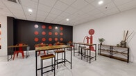 Located at 99 Pratt St in downtown Hartford, Connecticut, this single-floor commercial space makes a strong visual statement through a cohesive red and black design palette. The layout is open and versatile, centered around a communal area furnished with industrial-style high-top tables and matching stools crafted from reclaimed wood and black metal frames — ideal for collaborative work or casual gatherings.

The most eye-catching architectural feature is a dramatic black accent wall adorned with a grid of bold red circular discs, creating a graphic, contemporary focal point. Complementing this is a striking red vintage-style telephone wall mural, adding a playful nod to retro aesthetics. A separate, more intimate seating nook with a high-top table and open shelving displays decorative accents and greenery, offering a quieter setting within the space.

A vivid crimson red wall anchors the entryway, reinforcing the space's strong brand identity. Recessed display shelving with warm orange backlighting lines one wall, showcasing decorative objects and providing a curated, gallery-like touch. Light grey tile flooring runs throughout, providing a clean, neutral base that allows the bold color accents to stand out. A dropped grid ceiling with recessed lighting ensures the space is well-lit throughout. The overall ambiance is energetic, modern, and thoughtfully designed.
