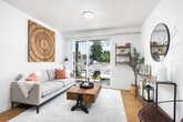 This thoughtfully designed single-floor residence offers a clean, contemporary aesthetic throughout. The open-concept kitchen is a standout feature, showcasing two-tone cabinetry with white upper cabinets and dark lower cabinets, stainless steel appliances including a refrigerator and range, light quartz countertops, and a peninsula island with bar seating illuminated by pendant lighting — ideal for both meal prep and casual dining. Warm wood-tone flooring flows through the kitchen and living areas, adding a natural, welcoming feel.

The living room is bright and airy, anchored by large sliding glass doors that open onto a private outdoor patio, allowing generous natural light and views of the surrounding landscape. Wall-mounted open shelving adds functional character to the space.

The bedroom offers plush carpeting, a large window with outdoor views, a soft green accent wall, and ample room for a full furniture arrangement. The bathroom is designed with accessibility in mind, featuring grab bars, a shower-tub combination, wood-tone flooring, and a gray vanity with quartz countertops. A built-in niche shelf adds practical storage. Throughout the unit, the neutral color palette and modern finishes create a cohesive, move-in-ready living environment.