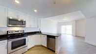This 2-bedroom, 2-bathroom single-floor residence offers a thoughtfully designed open-concept layout that seamlessly connects the kitchen and living areas. The kitchen is a standout feature, showcasing crisp white shaker-style cabinetry with sleek silver hardware, striking dark granite countertops, and a full suite of stainless steel appliances, including a range, built-in microwave, and dishwasher. A peninsula-style counter extension provides a natural transition into the open living space, making the area ideal for both everyday living and entertaining. The light wood-tone flooring runs throughout, adding warmth and visual continuity across the space. Recessed lighting in the kitchen and flush-mount fixtures in the living area ensure well-distributed illumination throughout. The living area is bathed in natural light, courtesy of large sliding glass doors fitted with vertical blinds that offer both privacy and access to outdoor space. The clean white walls and neutral palette throughout create a bright, airy ambiance that feels welcoming and move-in ready. The overall design balances modern aesthetics with functional living across two bedrooms and two full bathrooms.