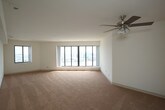 Located at 1 Harbor Ct in Portsmouth, Virginia, this single-floor residence offers an impressive combination of waterfront views and functional living spaces. The layout is anchored by a generously sized living area featuring warm carpeted flooring, crisp white walls, and a ceiling fan with light fixture. Floor-to-ceiling panoramic windows frame breathtaking views of the harbor and the Norfolk skyline, flooding the space with abundant natural light throughout the day.

The kitchen is thoughtfully designed with white cabinetry offering ample storage, granite-style countertops, tile flooring, and a full suite of white appliances including a range with oven, built-in microwave, and dishwasher. A stainless steel sink completes the functional workspace.

The bedroom continues the waterfront theme, featuring the same large multi-panel windows that capture sweeping harbor vistas. Soft carpeting and clean white walls create a calm, restful atmosphere. A hallway leads to a well-organized walk-in closet with built-in shelving, providing excellent storage capacity. The bathroom is finished with white tile flooring and includes a full soaking tub with tub-surround and brushed nickel fixtures. This residence delivers a serene, light-filled environment with remarkable water views at every turn.