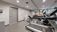 Located at 2670 Library Lane in North Vancouver, BC, this fitness center is a thoughtfully designed exercise space that maximizes its compact footprint with a well-rounded selection of equipment. The room features a clean, modern aesthetic with neutral-toned walls, recessed ceiling lighting, and large wall-to-wall mirrors that visually expand the space and allow users to monitor their form during workouts.

The cardio section is equipped with treadmills, elliptical trainers, a stationary bike, and a recumbent cycle, catering to a variety of cardiovascular training preferences. A wall-mounted flat-screen television is positioned for convenient viewing during cardio sessions. The free weights area includes a full rack of dumbbells in graduated sizes, accompanied by an adjustable workout bench and stability balls, providing options for strength and functional training.

A standout design element is the motivational typography mural that spans a prominent wall, featuring aspirational phrases in bold, multicolored text, adding an energetic and inspiring ambiance to the space. Built-in cubbies offer convenient storage for personal items. Natural light filters through a window, complementing the bright recessed lighting overhead. The durable flooring and organized layout ensure both safety and functionality throughout the room.