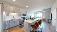 Located in the vibrant North Loop neighborhood of Minneapolis, this thoughtfully designed one-bedroom, two-bathroom residence offers a contemporary open-concept layout that maximizes every square foot. Light hardwood flooring flows throughout the main living areas, creating a warm and cohesive aesthetic.

The kitchen is a standout feature, outfitted with grey shaker-style cabinetry, a classic white subway tile backsplash, quartz countertops, and a full suite of stainless steel appliances including a gas range, built-in microwave, dishwasher, and refrigerator. A central island with bar seating connects the kitchen seamlessly to the living area, making it ideal for entertaining.

The living room is bright and airy, anchored by a large picture window that frames sweeping city views and fills the space with natural light. The bedroom is a comfortable retreat, featuring plush carpeting, access to an en-suite bathroom, and a large window with an outdoor view. An in-unit stacked washer and dryer adds everyday convenience. Both bathrooms are finished with clean, modern fixtures and tiled shower surrounds. The overall ambiance is fresh and contemporary, reflecting the best of modern urban living in Minneapolis.
